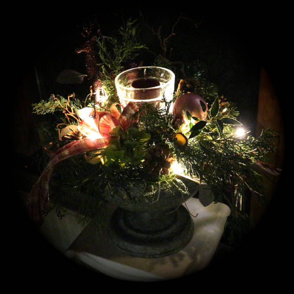 Beleuchtetes Adventsgesteck mit Kerzen-Glas im Zentrum.