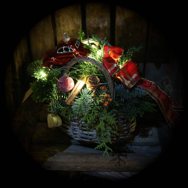 Beleuchtetes Adventsgesteck mit roter Schleife und rotem Auto in einem Korb. 