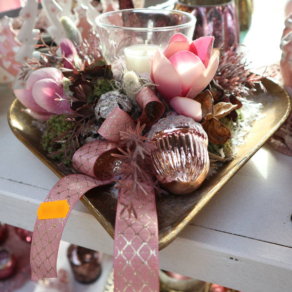 Eine schön dekorierte, messingfarbene Schale. Die zentrale Kerze wird von winterlicher Dekoration in rosa Farbtönen umgeben. Schöne Tischdekoration für die Adventszeit und zu Weihnachten.