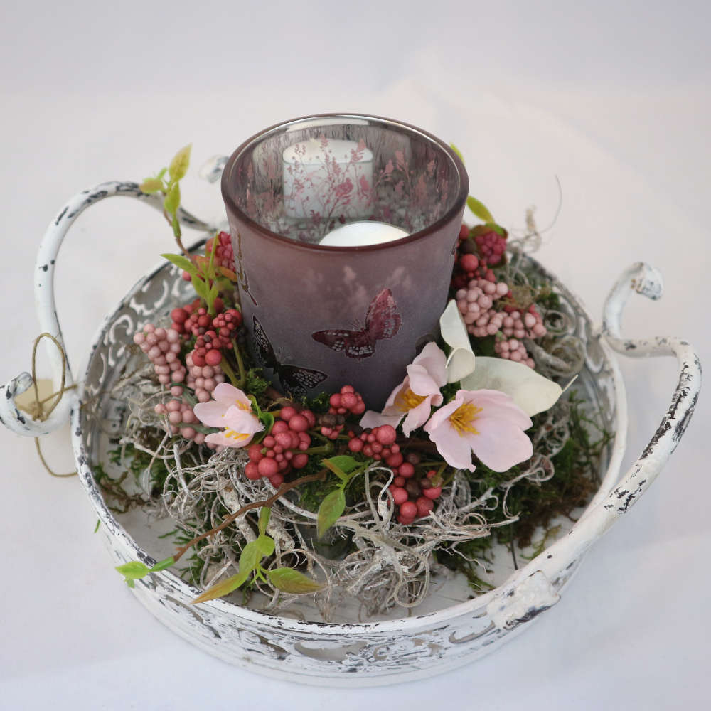  Ein weißes Tablett, dekoriert mit einem Kerzenglas und Kunstblumen sowie -beeren. 