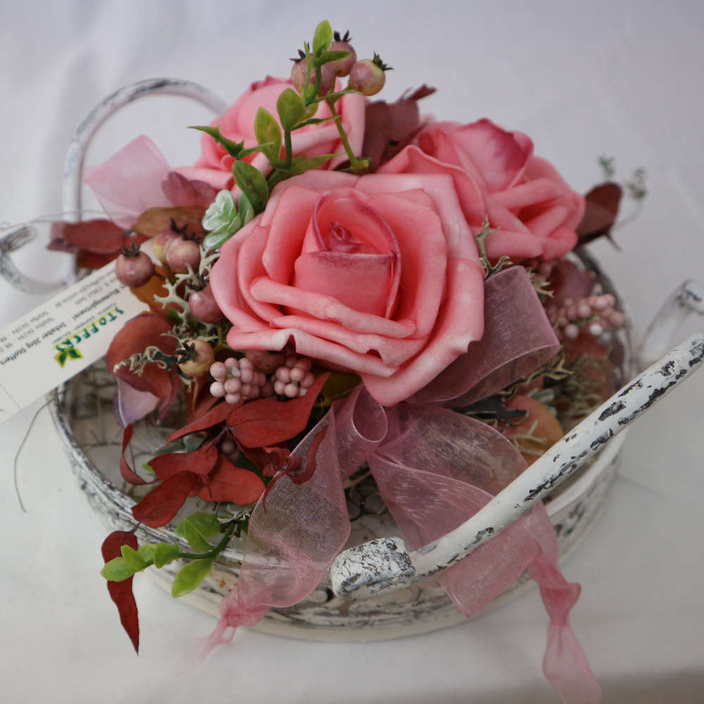 Ein Dekotablett im Vintage-Stil, welches mit Kunstblumen und Kunstbeeren in rosa dekoriert wurde.