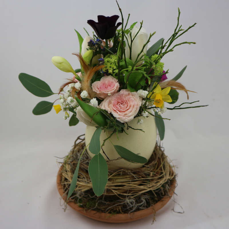 Ein farbenfroher Blumenstrauß aus Rosen, Tulpen und Frühblühern in einem Straußenei.