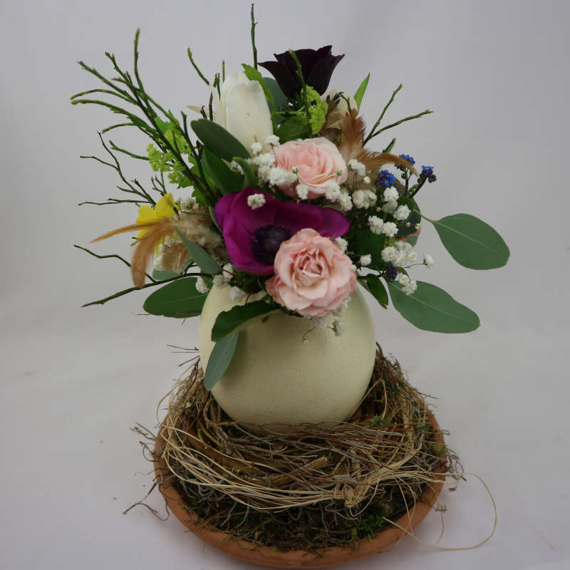 Ein farbenfroher Blumenstrauß aus Rosen, Tulpen und Frühblühern in einem Straußenei.