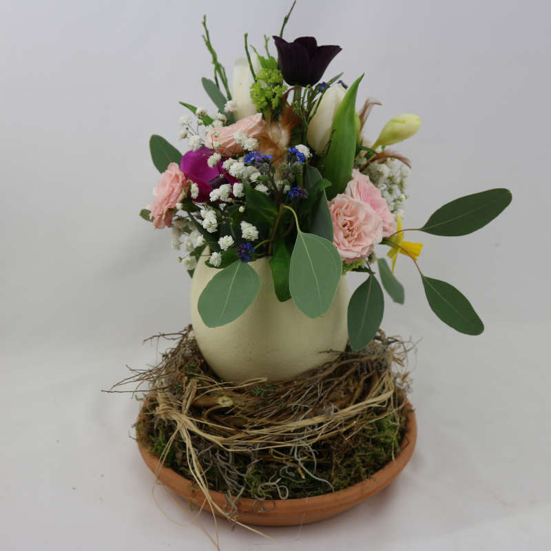 Ein farbenfroher Blumenstrauß aus Rosen, Tulpen und Frühblühern in einem Straußenei.
