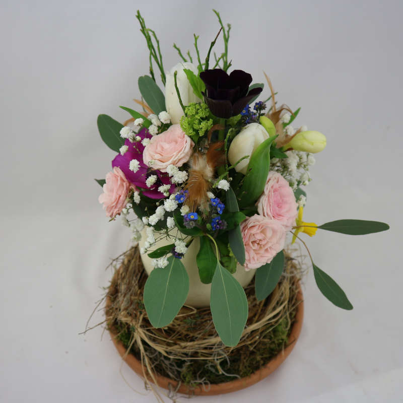 Ein farbenfroher Blumenstrauß aus Rosen, Tulpen und Frühblühern in einem Straußenei.