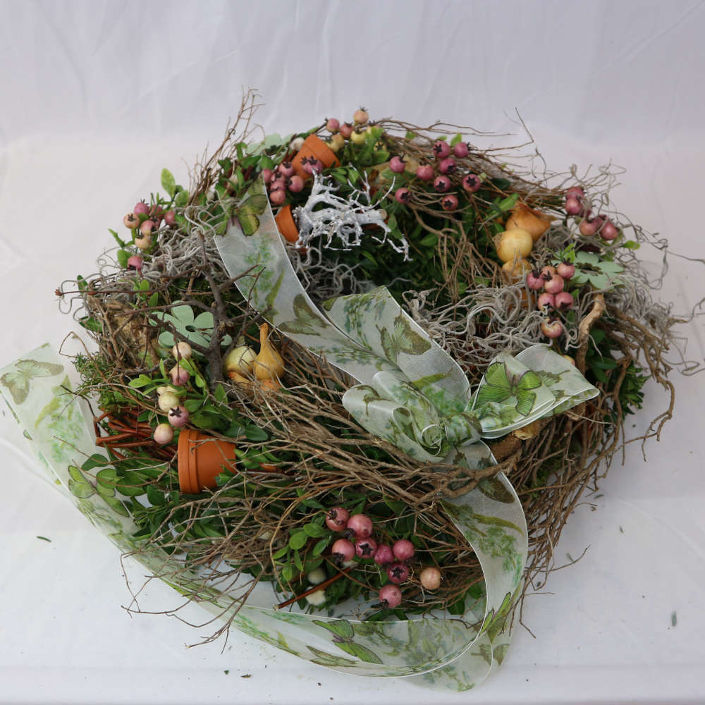 Ein rustikaler Kranz zum Hinlegen oder Anhängen. Bestehend aus Moos, Frühlingszweigen, rosa Kunstbeeren und Minitöpfchen.