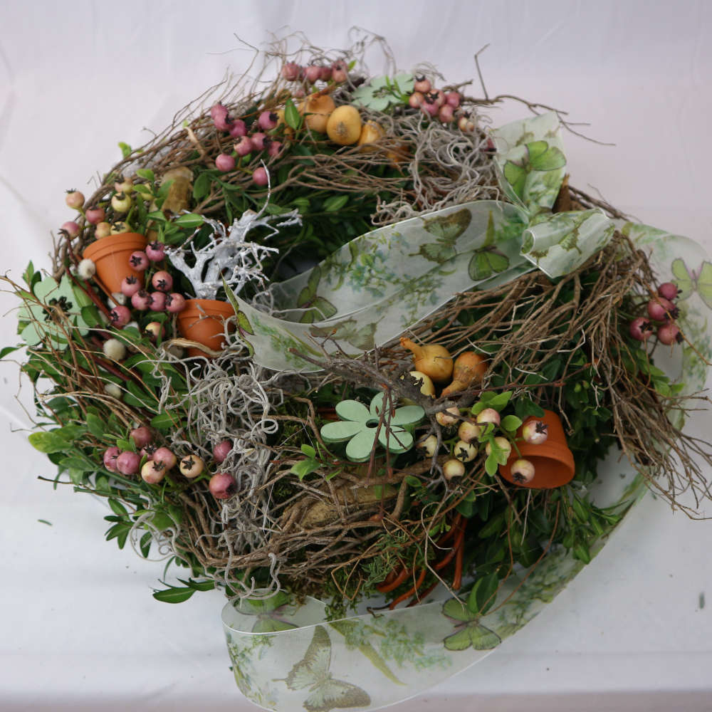 Ein rustikaler Kranz zum Hinlegen oder Anhängen. Bestehend aus Moos, Frühlingszweigen, rosa Kunstbeeren und Minitöpfchen.