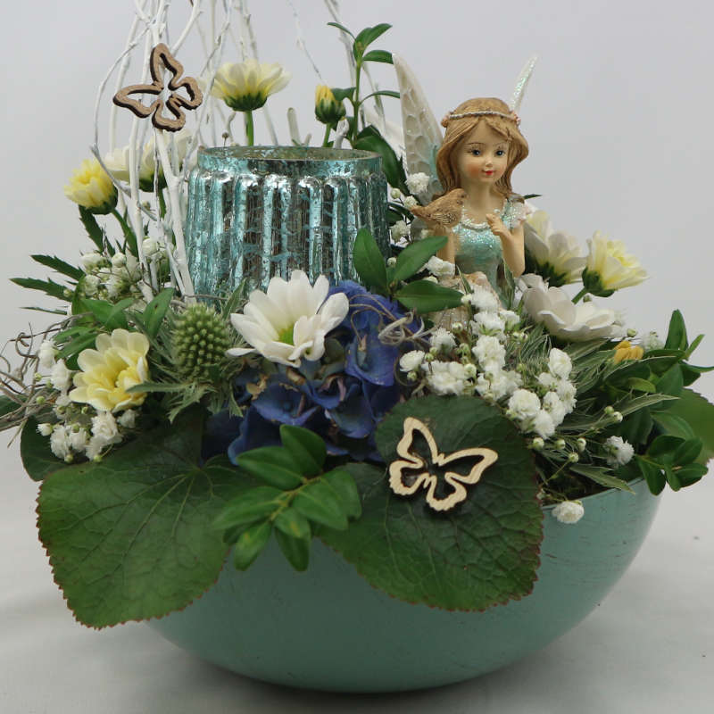Ein sattgrünes Gesteck aus Frischblumen mit einer mintgrünen Elfe und einem Kerzenglas.