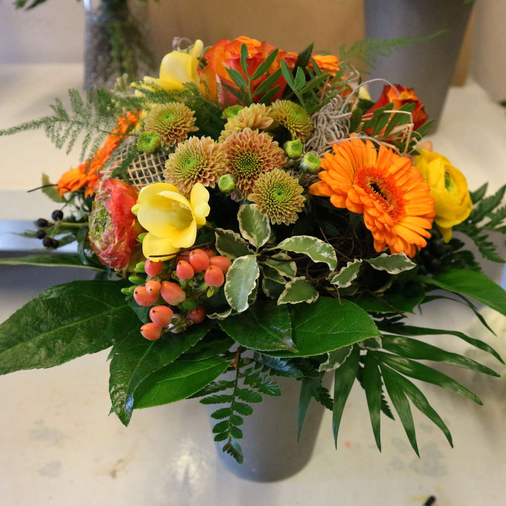 Ein großer, kompakt gebundener Blumenstrauß, bestehend aus orangen Gerbera und orange-gelben Rosenblüten; ergänzt um gelbe Blüten.
