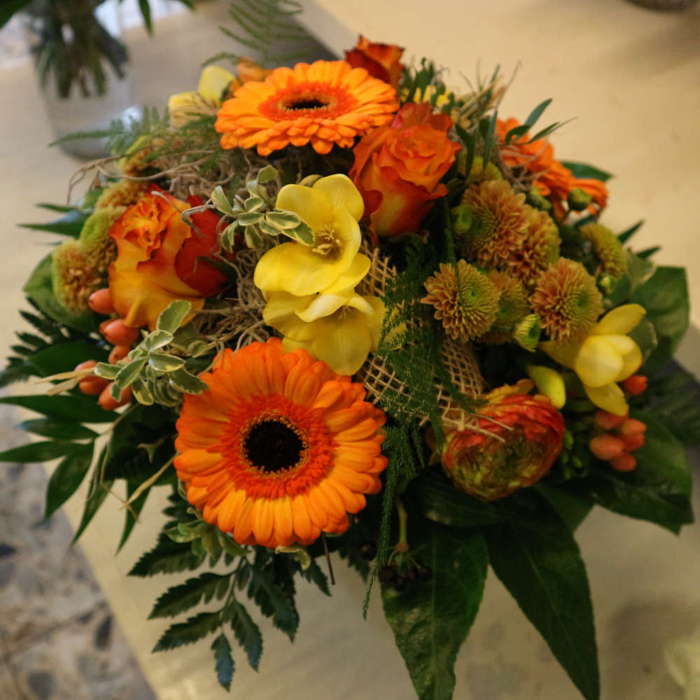 Ein großer, kompakt gebundener Blumenstrauß, bestehend aus orangen Gerbera und orange-gelben Rosenblüten; ergänzt um gelbe Blüten.