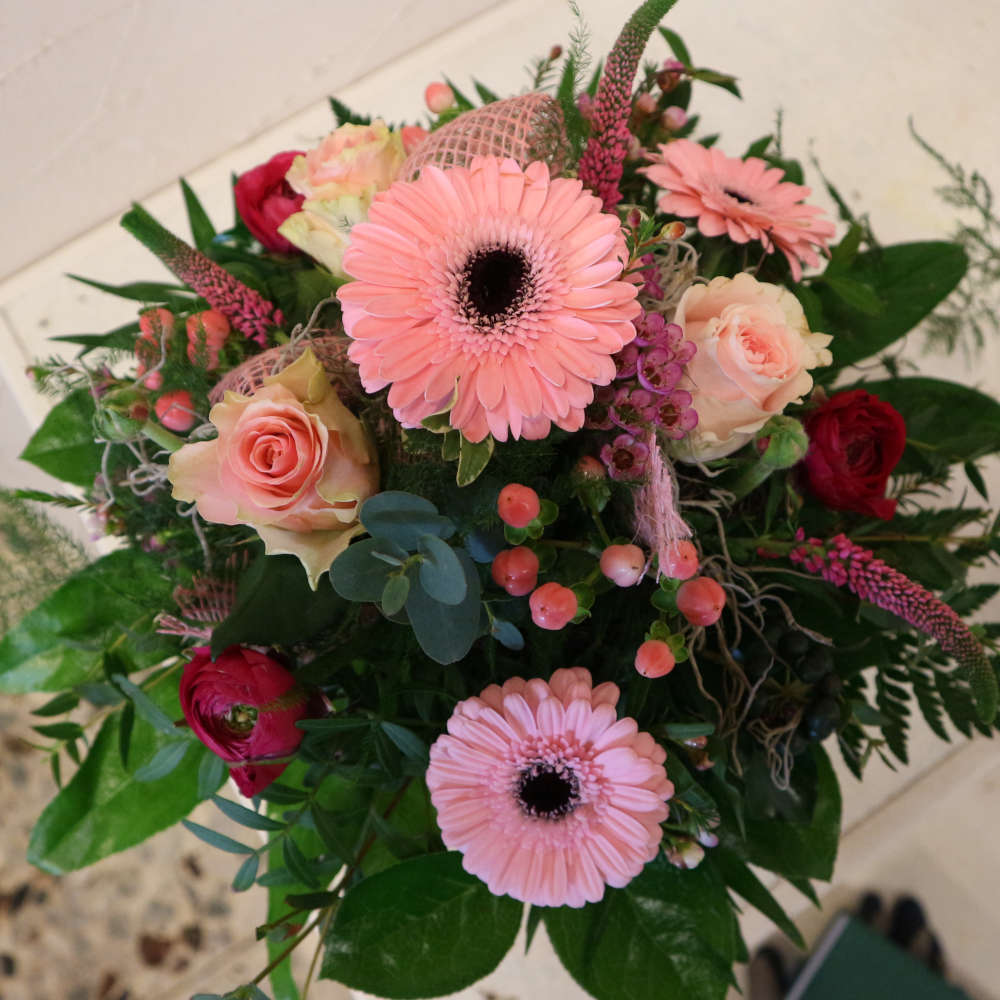  Ein großer, kompakt gebundener Blumenstrauß, bestehend aus rosa Gerbera, aufstrebenden Veroknika und rosa Rosenblüten. 