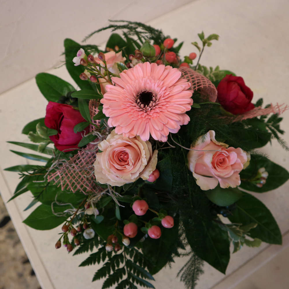 Ein kleiner, kompakt gebundener Blumenstrauß, bestehend aus rosa Gerbera, aufstrebenden Veroknika und rosa Rosenblüten.
