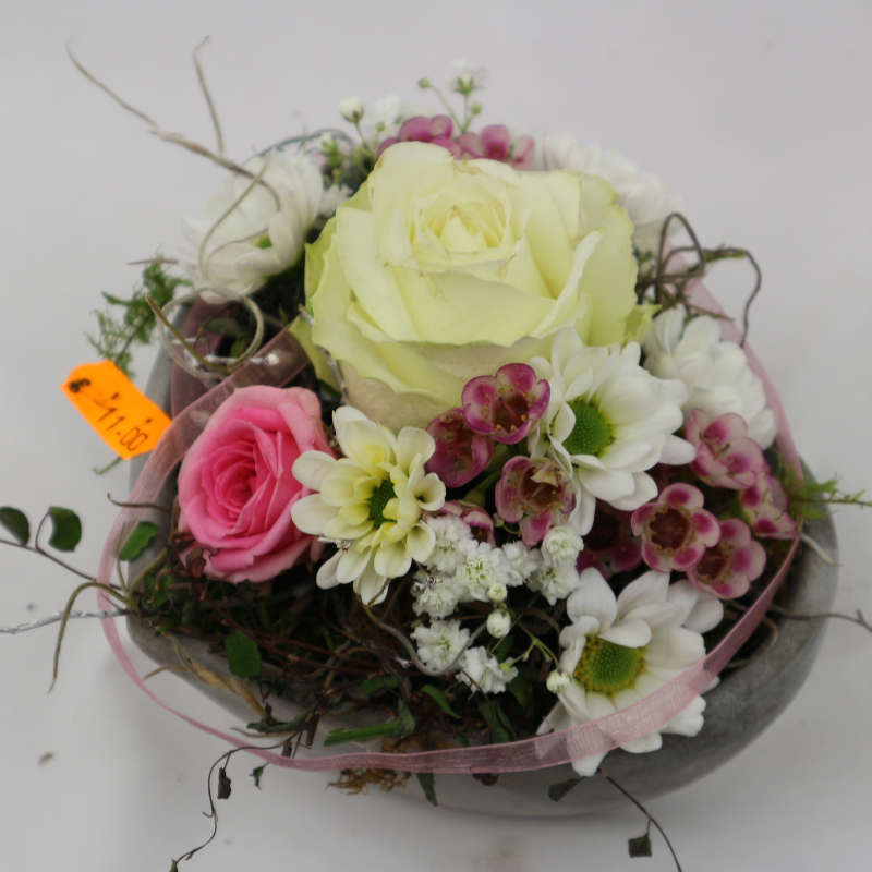  Eine kleines Gesteck in Herzform bestehend aus rosa und weißen Rosenblüten sowie Bonnies. 