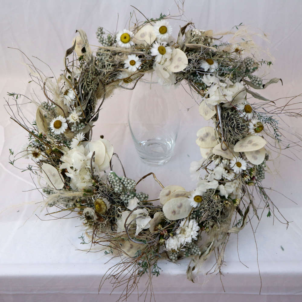  Ein weißer Kranz aus getrockneten Blumen. Unter anderem wurden Strohblumen und Hortensieblüten verwendet. Locker gewickelte Variante. 