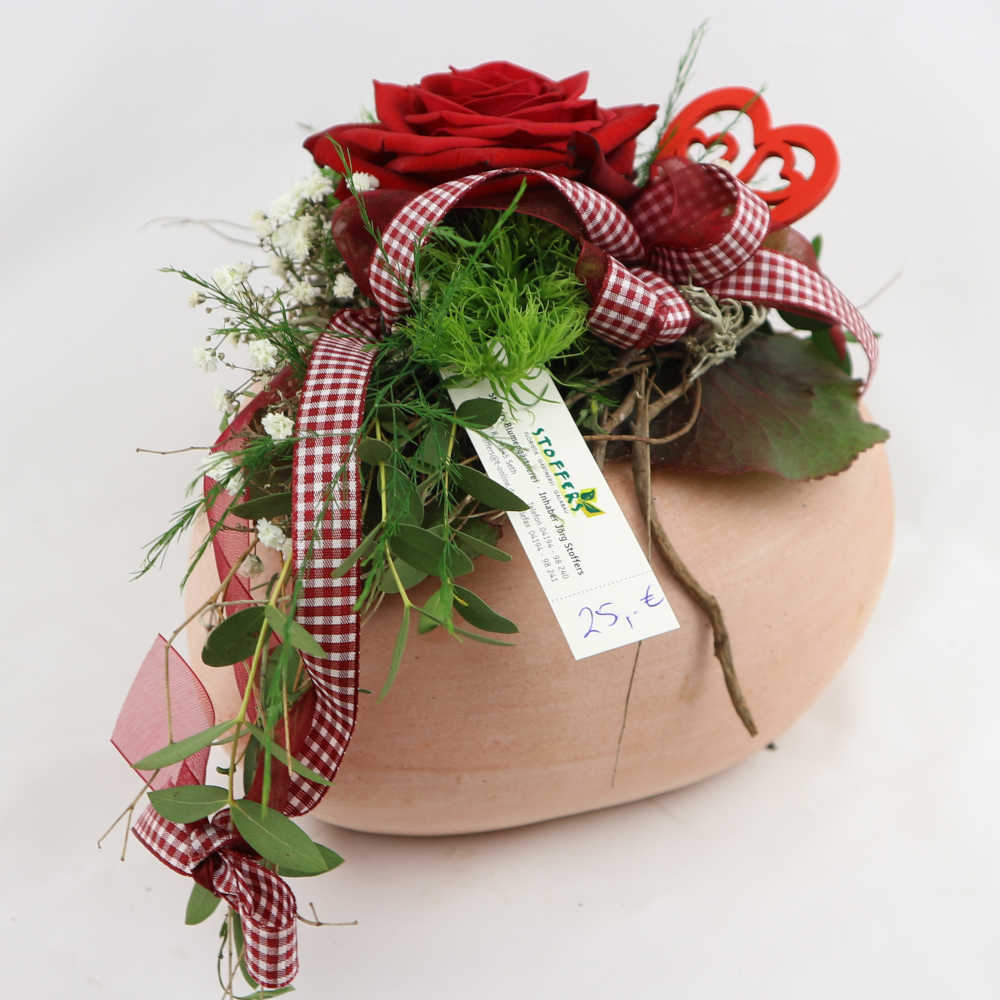 Ein Herz aus Ton, besteckt mit einer roten Rose, Schleierkraut und Nelken. Kann eingetrocknet werden.
