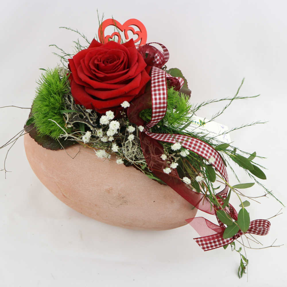 Ein Herz aus Ton, besteckt mit einer roten Rose, Schleierkraut und Nelken. Kann eingetrocknet werden.