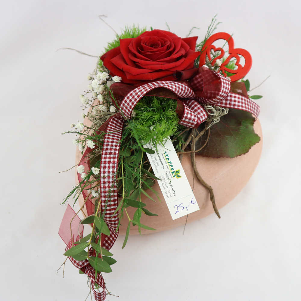 Ein Herz aus Ton, besteckt mit einer roten Rose, Schleierkraut und Nelken. Kann eingetrocknet werden.